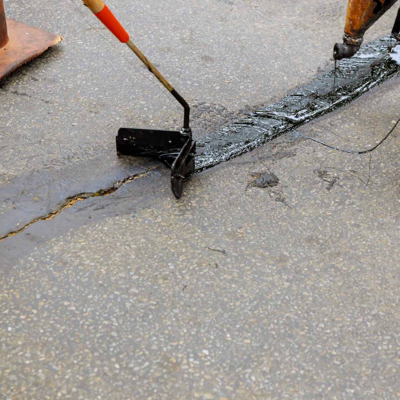 Road surface restoration work in the worker performs on road patcher work on the repair of cracks by filling and sealing with coated by bitumen emulsion asphalt surface.