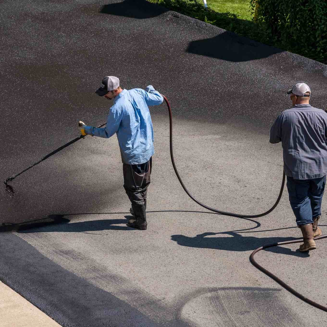 Morgantown, West Virginia - 3 June 2019: Workers applying blacktop sealer to asphalt street using a spray
